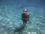 Homem mergulhador de pé debaixo de água e olhando para a câmera — Fotografia de Stock