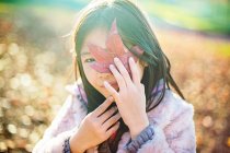 Menina escondendo rosto atrás de uma folha na natureza — Fotografia de Stock