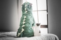 Задній вид шарпей в динозавра костюм і кошеня дивлячись через вікно — стокове фото