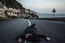 Mulher deitada no meio da estrada costeira — Fotografia de Stock