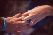 Imagen recortada de pareja con anillos de boda tomados de la mano contra el fondo borroso - foto de stock