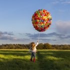 Mädchen spaziert mit bunten Luftballons auf Wiese — Stockfoto