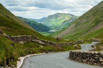 Winding road and stone wall along mountains, United Kingdom, England, Cumbria, Lake District — Stock Photo