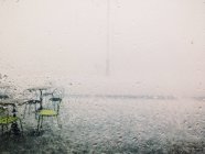 Vista através de vidro de cadeiras molhadas e mesas na chuva — Fotografia de Stock