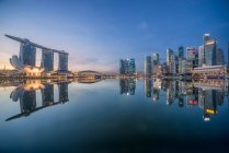 Singapur, Rascacielos frente al mar reflejándose en el puerto todavía por la noche - foto de stock