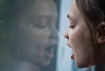 Крупним планом мила дівчинка дихає на вікно з відображенням — стокове фото