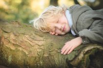 Sorrindo menino loiro cochilando no tronco da árvore — Fotografia de Stock