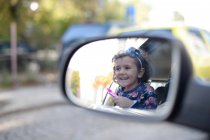 Little girl enjoying car trip and looking in rear view mirror — Stock Photo