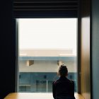Visão traseira da menina olhando pela janela — Fotografia de Stock