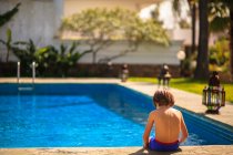 Boy sitting on edge of swimming pool in summer — Stock Photo