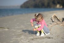 Little girl playing with stick on sandy beach — Stock Photo