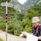 Hiker on mountain trail looking at map near direction sign, Spain, Catalonia, Tarragona, Priorat, Ulldemolins — Stock Photo