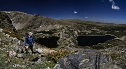Uomo in piedi tra le rocce sul fianco della montagna con tre laghi sullo sfondo, Stati Uniti, Colorado, Montagne Rocciose — Foto stock