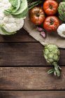 Cauliflower, artichokes, asparagus, garlic and tomatoes on wooden table — Stock Photo