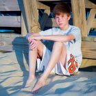 Young boy sitting on sandy beach and leaning against boardwalk — Stock Photo