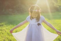 Chica sosteniendo dobladillo de vestido en la luz del sol al aire libre - foto de stock