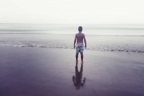 Вид ззаду без сорочки Самотній хлопчик стоїть на пляжі — стокове фото