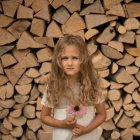 Retrato de menina segurando flor rosa contra pilha de logs — Fotografia de Stock