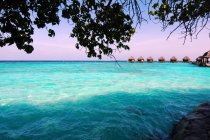 Aguas turquesas y cabañas de playa en el horizonte, Maldivas - foto de stock