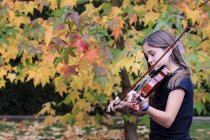 Mädchen spielt Geige mit Herbstlaub auf dem Hintergrund — Stockfoto