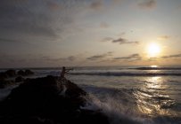 Ecuador, Man fishing on rock in Pacific Ocean at sunset — Stock Photo