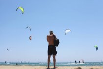 Вид сзади человека, стоящего на пляже и смотрящего на воздушных змеев — стоковое фото