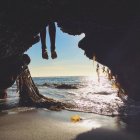 Cropped image of person legs hanging in front of cave entrance on beach — Stock Photo