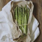 Fresh asparagus wrapped in paper on white cloth — Stock Photo