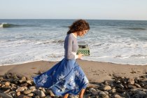 Mulher vestindo vestido andando ao longo da praia com máquina de escrever — Fotografia de Stock