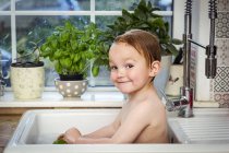 Mignon petit garçon prenant bain dans l'évier de la cuisine et regardant la caméra — Photo de stock
