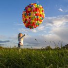Girl standing with colorful balloons in meadow — Stock Photo