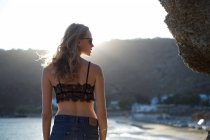 Rückansicht einer Frau mit Spitzenoberteil, die am Strand steht und über die Schulter schaut — Stockfoto