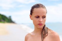 Retrato de la mujer pensativa de pie en la playa y mirando hacia los lados - foto de stock