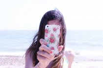 Девушка-подросток фотографируется со смартфоном на пляже — стоковое фото