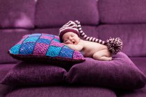 Sleeping baby girl wearing funny hat lying on stacked cushions — Stock Photo