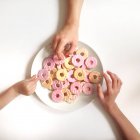 Vista dall'alto di mani umane che prendono biscotti dal piatto su sfondo bianco — Foto stock