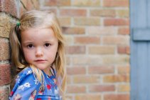 Portrait of blond girl leaning against brick wall — Stock Photo