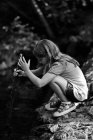 Mädchen steht auf Felsen und stochert Stock in Fluss — Stockfoto