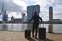 Paesi Bassi, Rotterdam, uomo d'affari in piedi con valigie sul lungomare della città — Foto stock