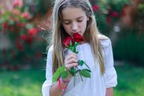 Chica oliendo rosas rojas en el jardín - foto de stock