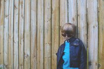 Boy wearing sunglasses posing against fence — Stock Photo