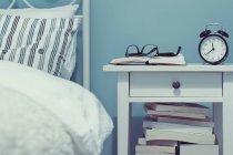 Закрытый вид на ночной стол с книгами и будильником — стоковое фото