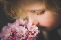 Primer plano de niña rubia oliendo flores - foto de stock