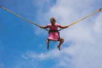 Дівчина стрибає на батуті з хмарним небом на фоні — стокове фото