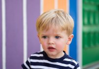 Toddler blond boy staring in front of rainbow wall — Stock Photo