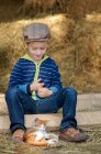 Мальчик в кепке играет с котенком на сене — стоковое фото