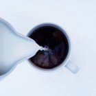 Vista aérea de la leche que se vierte en una taza de café - foto de stock