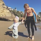 Zwei Brüder halten sich am Strand mit Surfbrett an den Händen — Stockfoto