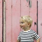 Portrait d'un garçon souriant debout devant une clôture rose — Photo de stock