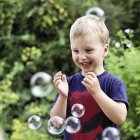 Glücklicher blonder Junge, der draußen mit Seifenblasen spielt — Stockfoto